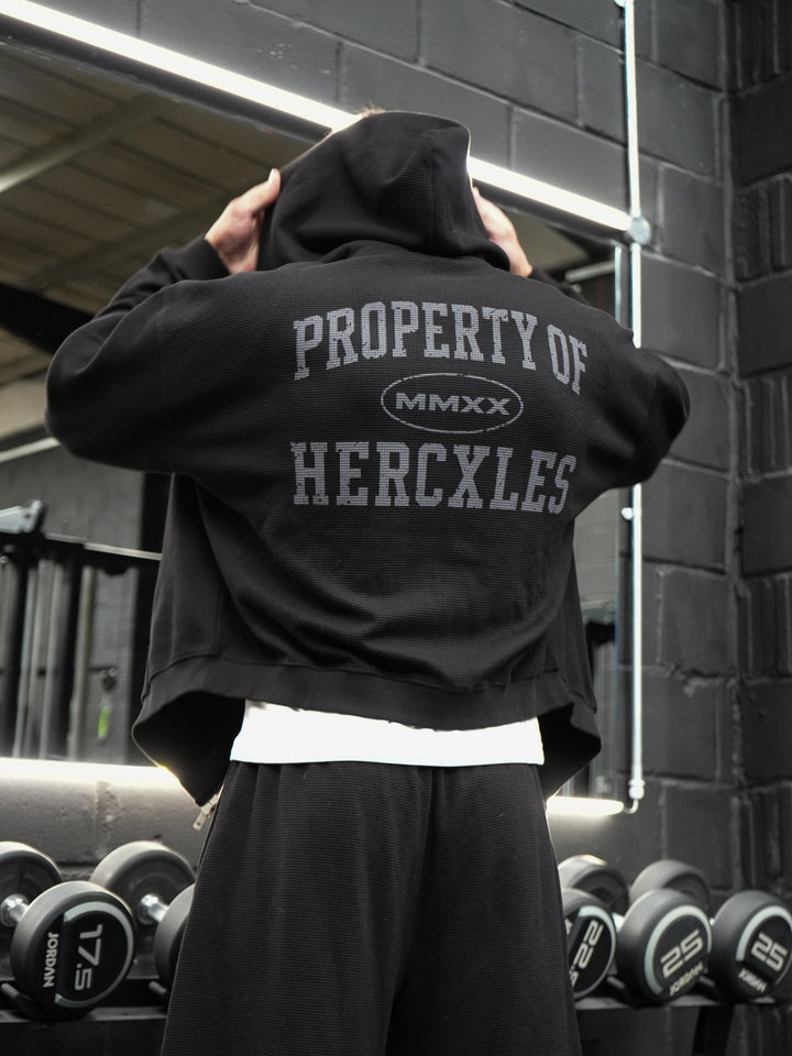 Athlete wearing a black waffle-texture HERCXLES Property Of hoodie and sweatpants from the back in the gym