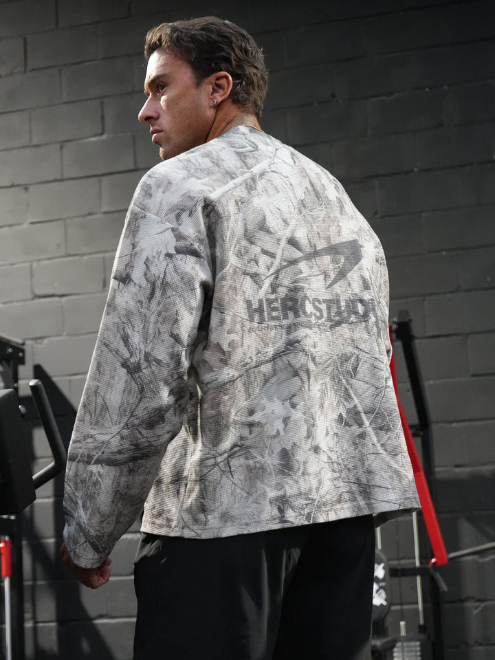 Athlete looking over his shoulder in a gym wearing a grey all-over-print HERCSTUDIOS long-sleeve shirt
