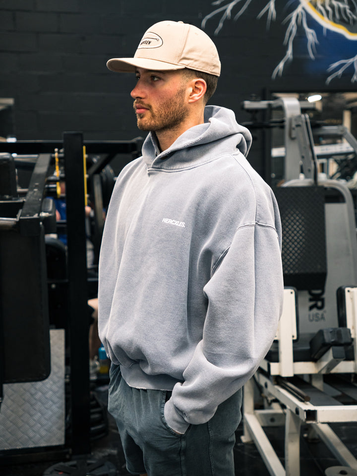 Athlete wearing a grey oversized HERCXLES hoodie and a cap in a gym