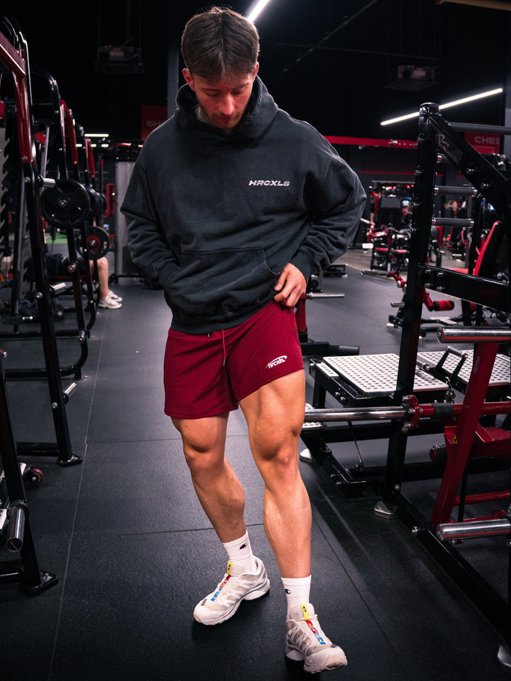 Athlete in a dark hoodie and red HERCXLES shorts posing in a gym