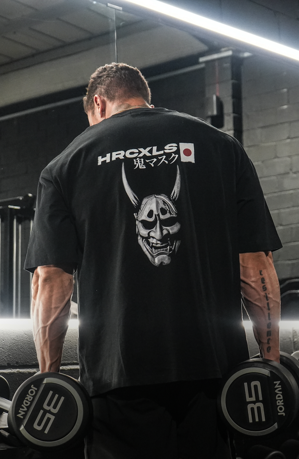 Model wearing a black HERCXLES Oni T-shirt from the back in the gym